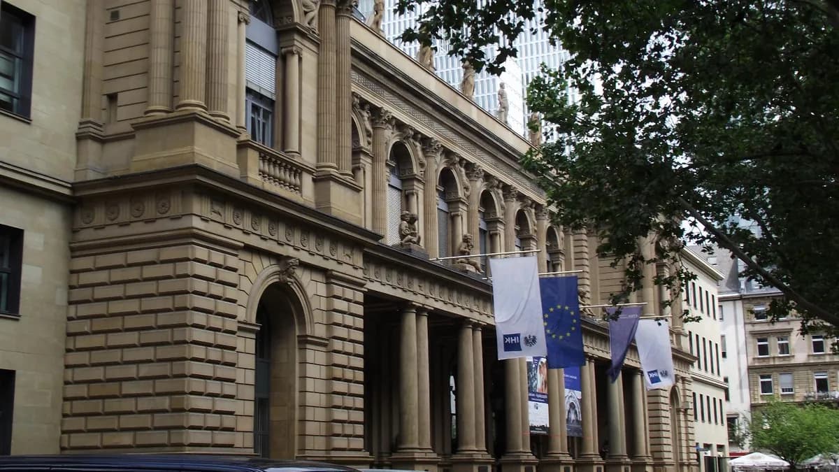 Die Fassade der Frankfurter Börse mit der EU-Flagge und Institutionsflaggen, davor einige parkende Autos (Symbolbild)
